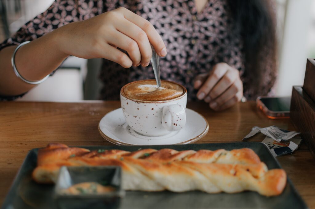A woman enjoying coffee and pastry at a café, stirring her drink while seated indoors.